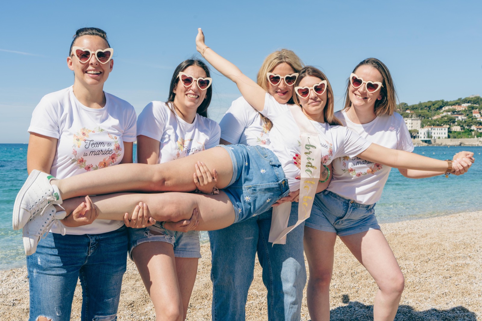 Groupe d'amies portant la future mariée en riant sur une plage lors d'un EVJF près d'Aix-en-Provence