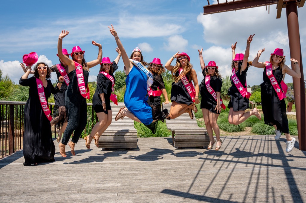 Groupe d'amies en casquettes roses sautant de joie lors d'un EVJF près d'Aix-en-Provence